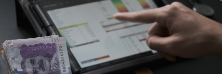A person reviewing a financial chart on a tablet with a stack of cash nearby